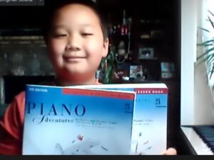 Online piano lessons student holding piano books